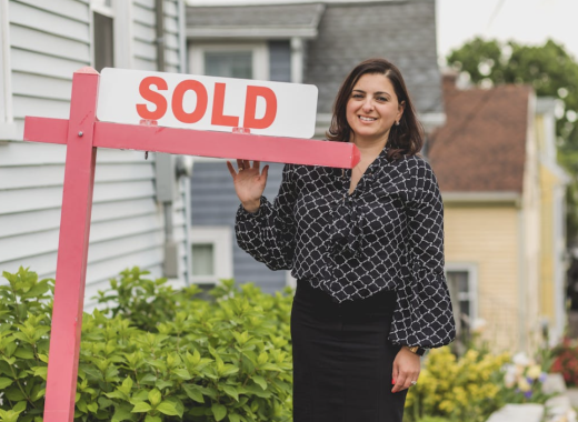 Smiling Female Real Estate Agent Standing Next to a Sold Sign